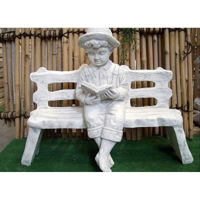 Steinfigur Junge sitzt auf einer Bank und liest ein Buch.